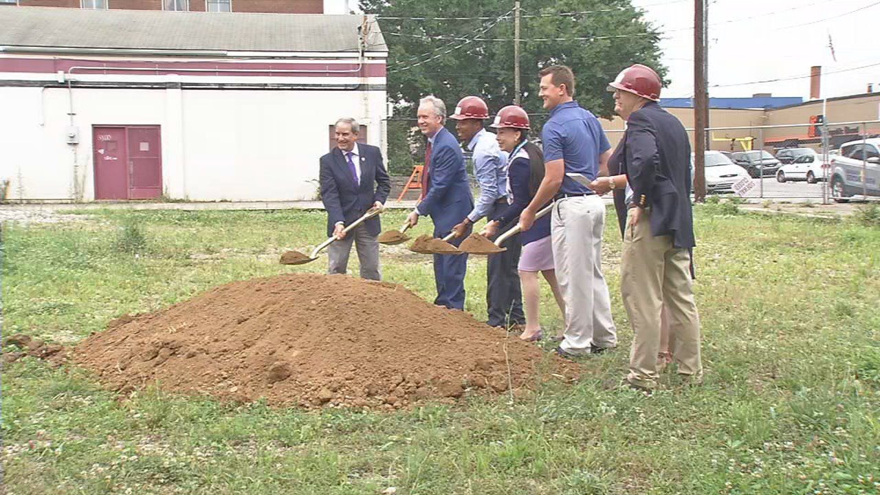 A team of individuals stands near a dirt pile, equipped with shovels, working together on a digging project