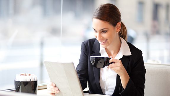 A businesswoman in a suit gazes at her laptop, holding a cup in her hand